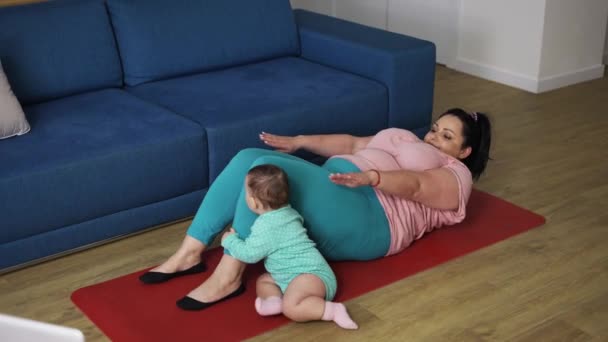 Överviktig kvinna gör buken övningar medan hennes barn leker bredvid henne — Stockvideo