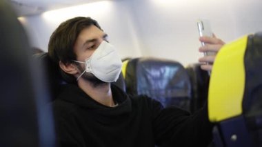 Pandemik zamanlarda uçakta seyahat eden solunum maskeli bir adam selfie çeker.