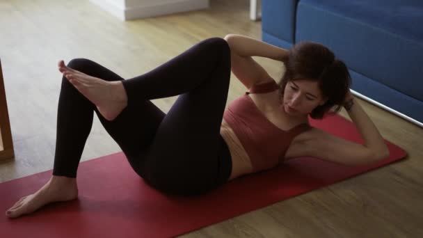Athletic girl in sportswear is pumping the abdominals on mat at home — Stock Video