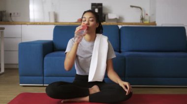 Afrika kökenli Amerikalı kadın, yoga minderinde antremandan sonra su içiyor.