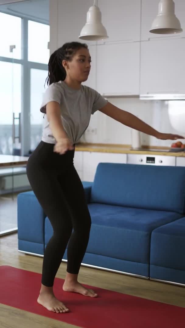 Afroamericana joven deportista haciendo sentadillas en una alfombra en casa — Vídeos de Stock