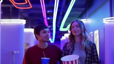 Mutlu genç kadın ve adam bir kova patlamış mısır ve içkiyle yürüyüp sinemada sohbet ediyorlar.