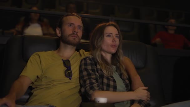Blonde girl looking scary while watching film, her boyfriend calming her down — Stock Video
