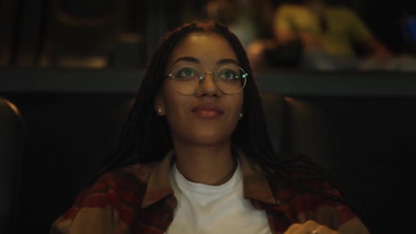 Mujer afroamericana sentada en sillón viendo una comedia en el cine, comiendo palomitas de maíz — Vídeo de stock