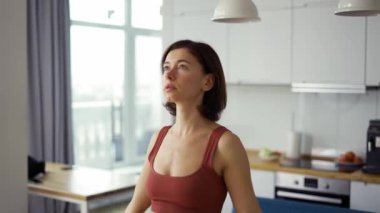 İnce bir kadın, parlak bir odada, namaste 'de el ele tutuşarak asanas gibi duruyor.