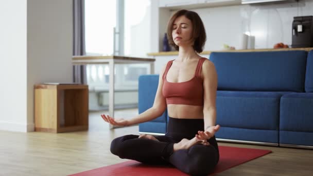 Портрет женщины, делающей упражнения для йоги с лотосом на коврике для йоги дома утром — стоковое видео