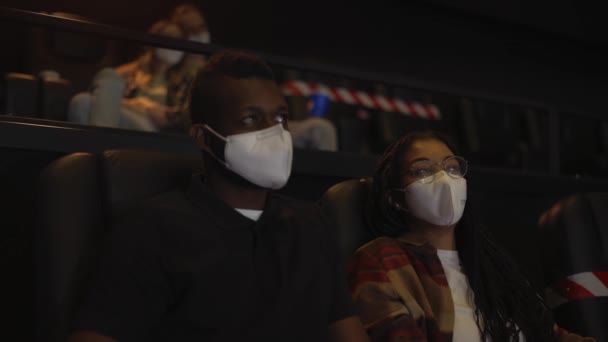 Casal afro-americano desfrutando de filme durante pandemia, vestindo máscaras brancas — Vídeo de Stock