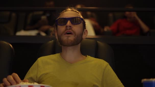 En man i 3D-glasögon tittar på film på bio och äter popcorn — Stockvideo