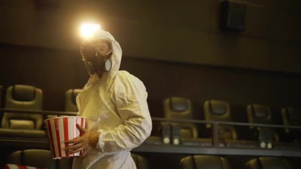 Un hombre con traje de protección blanca y respirador vino solo al cine con un cubo de palomitas de maíz — Vídeo de stock