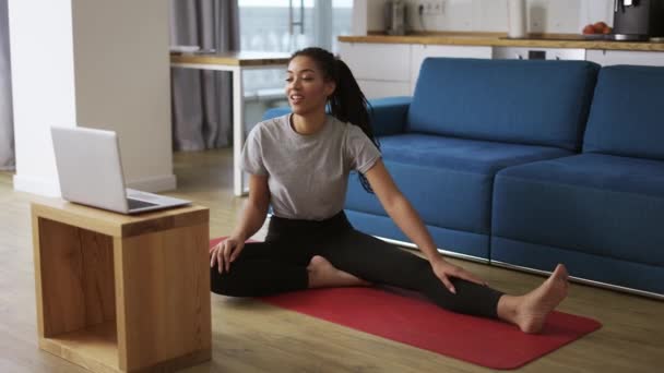 Sportowa Afroamerykanka ćwiczy, ćwiczy rozciąganie na macie do jogi oglądając filmy fitness — Wideo stockowe