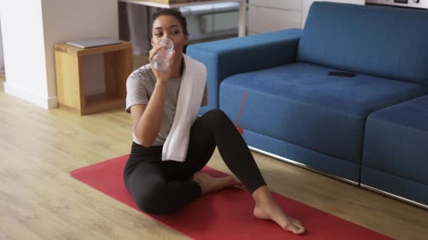 Sportowa Afroamerykanka pijąca wodę po treningu w domu na macie do jogi — Wideo stockowe