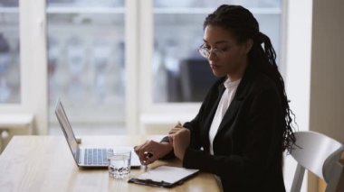 Afro-Amerikalı sekreter kız ofis masasında dizüstü bilgisayar kullanarak oturuyor.