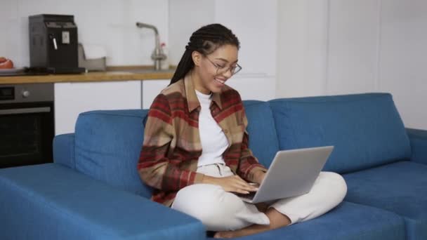 Pozytywna dziewczyna z dredami śmieje się i uśmiecha z laptopem na kolanach — Wideo stockowe