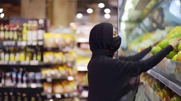 Müslüman kadınlar bakkal alışverişi yapıyor, raftan meyve alıyor, yandan bakıyor. — Stok video