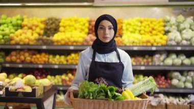 Başörtüsü içinde Müslüman bir kadın markette bir sepet taze sebzeyle yürüyor, ağır çekimde.