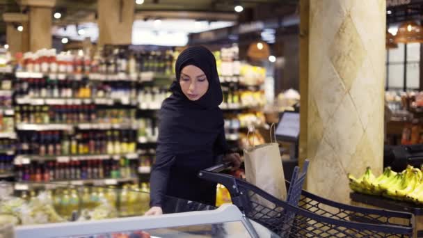 果物の通路からいくつかの果実を取って、食料品のためのイスラム教徒の女性のショッピング — ストック動画
