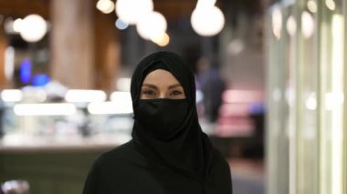 Markette alışveriş arabasıyla duran tesettürlü ve maskeli bir kadının portresi.