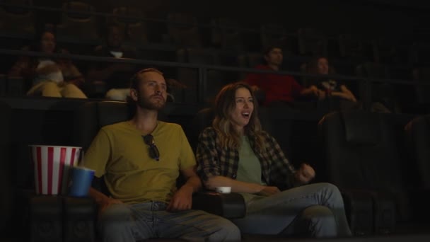 Piękna dziewczyna wygląda przerażająco oglądając film i przytulając się do swojego chłopaka siedzącego obok niej — Wideo stockowe