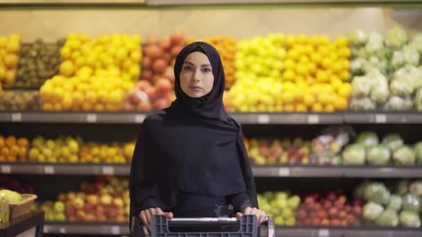 Retrato de una mujer musulmana comprando comestibles en el supermercado, empuje el carro — Vídeos de Stock