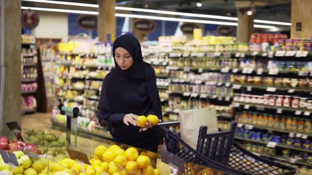 Μουσουλμάνα ψωνίζει για ψώνια, παίρνει λεμόνια από τον διάδρομο με τα φρούτα. — Αρχείο Βίντεο