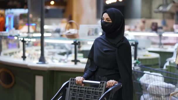 头戴头巾戴防护面具的女人在杂货店里推着购物车 — 图库视频影像