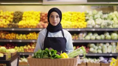 Markette bir sepet taze sebzeyle duran tesettürlü bir kadının portresi.