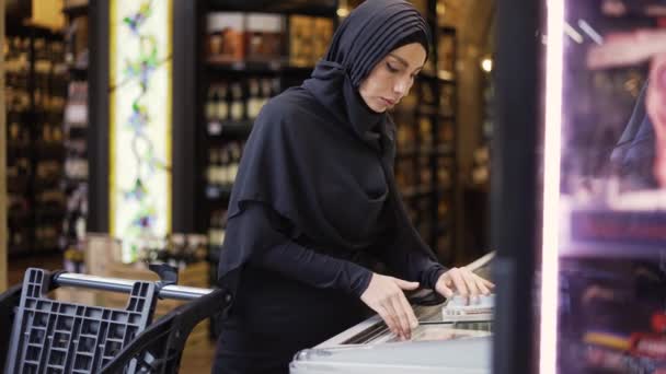 Woman in hijab and takes product from the freezer in suprmarket — Stock Video