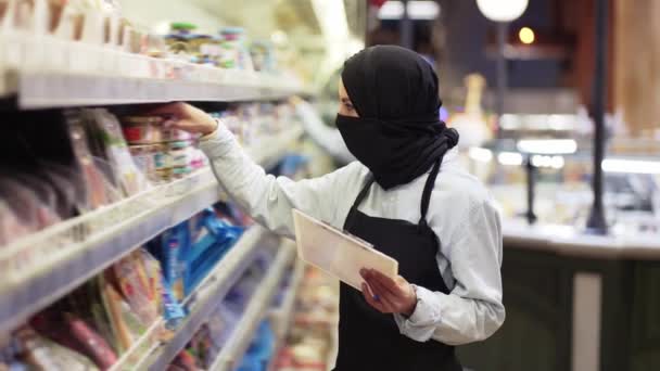 店で働く黒いスカーフの女性、タブレットで棚を検査 — ストック動画
