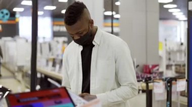 Afro-Amerikalı adam bir dükkandan yeni bir cep telefonu seçiyor, nasıl çalıştığını kontrol ediyor.