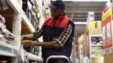 Erkek denetçi, üst raflarda merdiven kullanarak malları inceliyor.