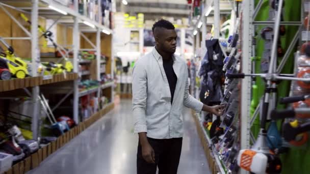Uomo afroamericano che cammina lungo gli scaffali in ferramenta ed esamina le merci — Video Stock