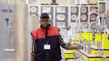 Satış elemanı ev hipermarketinde sıraların arasında kameraya bakıyor.