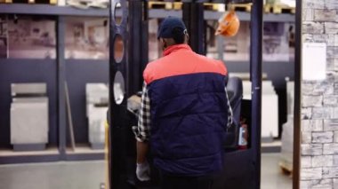 Depoda forklift operatörü, üniforması ve şapkası var.