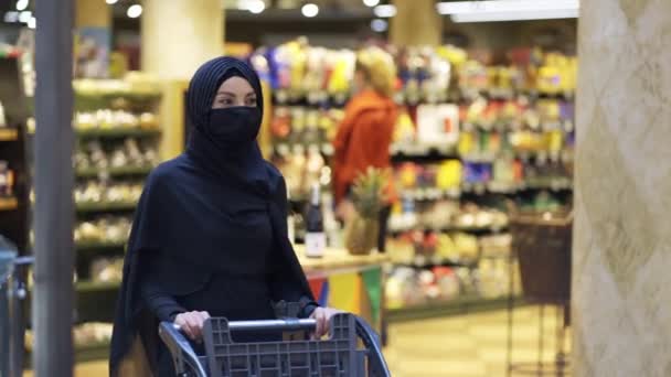 现代穆斯林妇女头戴头巾，在超市购物，挑选商品，戴口罩 — 图库视频影像