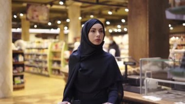 Türbanlı kadın süpermarketteki raftan bir sürü ürün alıyor.