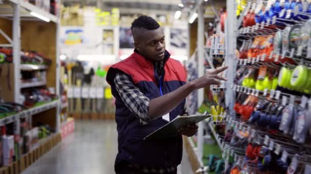 Man supervisor lopen tussen rijen in hardware winkel onderzoeken van goederen op planken met tablet — Stockvideo