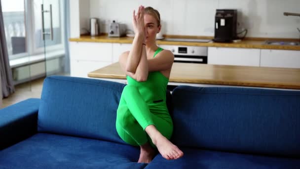 Mujer joven practicando la pose de águila en casa en el sofá — Vídeos de Stock