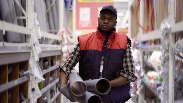 Рабочий ходит с водопроводными трубами в магазине сантехники или оборудования — стоковое видео