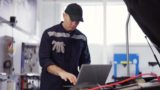 Retrato de mecánico utiliza un ordenador portátil durante la realización de pruebas de diagnóstico en el motor, cámara lenta — Vídeos de Stock