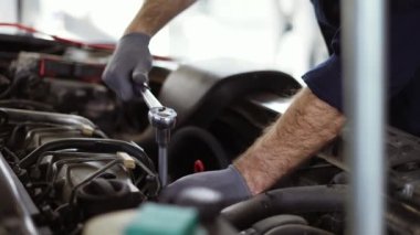 Araba tamircisi, araba servisindeki motoru tamir etmek için ingiliz anahtarı kullanıyor.