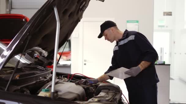 Mechanica in een auto reparatiewerkplaats controleren motor met behulp van een tablet — Stockvideo