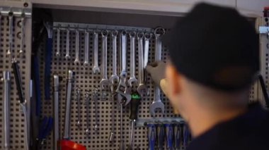 Bir araba tamircisi elinde İngiliz anahtarıyla tezgahın yanında duruyor.