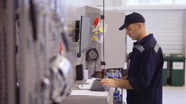 Üniformalı tamirci bozuk arabayı tamir etmek için bilgisayarı kullanıyor.