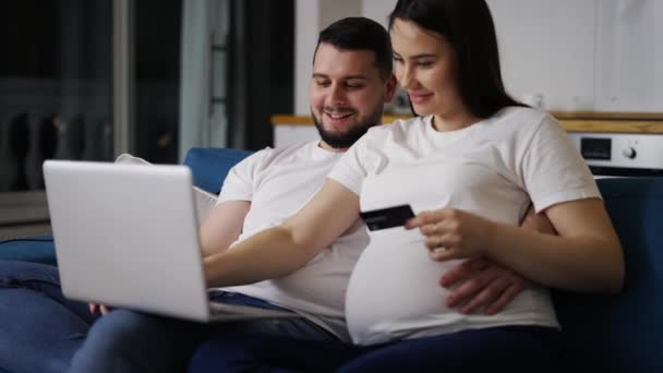 Casal esperando bebê, sentado no sofá em casa e compras on-line usando laptop — Vídeo de Stock
