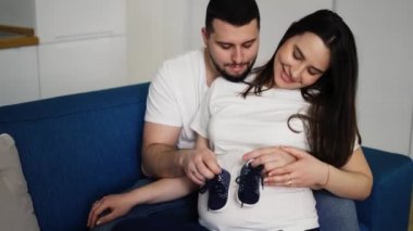 Güzel hamile kadın ve kocası karnında bebek ayakkabıları taşıyorlar.