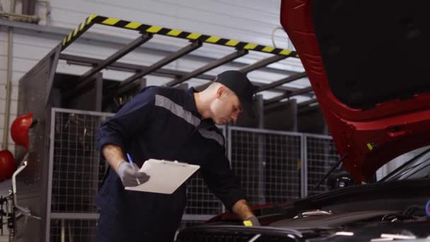 Mécanicien dans un atelier de réparation automobile vérifiant le moteur à l'aide d'une tablette, angle bas — Video