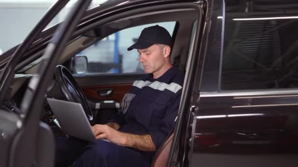 Mecánico que trabaja en el ordenador portátil en el servicio de reparación de automóviles dentro del coche, de cerca — Vídeo de stock