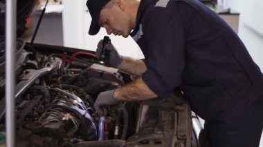 Motoru el feneriyle kontrol eden araba servisi çalışanı.