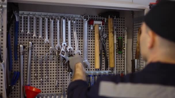 Ein Automechaniker steht mit einem Schraubenschlüssel in der Nähe des Stands, nimmt die benötigte Größe an, Zeitlupe — Stockvideo