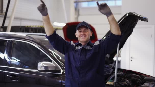 Sorrindo mecânico homem de uniforme e luvas dançando engraçado em um centro de auto serviço moderno — Vídeo de Stock